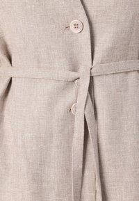 Beige Leinenblazer mit strukturiertem Finish, der zwei Knöpfe und eine gebundene Taillenpartie für den Verschluss aufweist.
