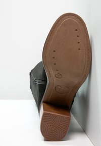 Bottine noire à cheville avec une tige texturée et une semelle extérieure en caoutchouc marron unie. La semelle présente un motif étoile et des d étails de marquage embossés.