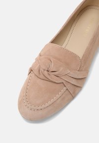 Mocassins en daim couleur nude avec un nœud décoratif, une surpiqûre contrastante et un design à bout arrondi. Texture douce avec une doublure lisse.