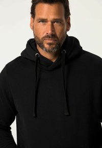 Felpa nera con cappuccio e coulisse, dal tessuto morbido e dal design minimalista, con una vista frontale di un uomo con la barba.