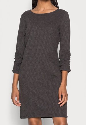 Žena oblečená v těsně přiléhajících dlouhých rukávech tmavě šedých texturovaných šatech s kulatým výstřihem a nabránými rukávy.