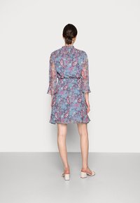 Sininen kukkamekko paisley-kuvalla, läpikuultavat pitkät hihat, röyhelökaulus ja vyötärösolki. Helma ulottuu polvien ylle. Yhdistetty kevyisiin sandaaleihin.