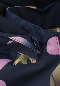 Marinblått tyg med rosa och gula abstrakta mönster. Fiskbensstruktur med knappstängning och sydda detaljer. Mjuk foder synligt.