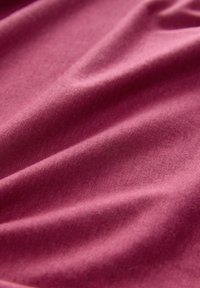 Miękka burgundowa tkanina o gładkiej teksturze, z delikatnymi fałdami i zagnieceniami, wskazującymi na elastyczność i wagę. Odpowiednia do odzieży lub tapicerki.