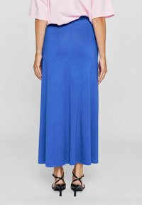 Maxikleid aus blauem Jersey mit glatter Textur, verfügt über eine taillierte Taille und einen fließenden Saum. Kombiniert mit schwarzen Riemchensandaletten.