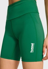Gröna idrottsshorts med hög midja, tillverkade av elastiskt material, med vit "hummel PERFORMANCE"-logotyp på sidan.