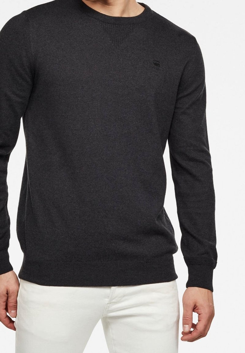 Pull à col rond gris foncé en matière douce, doté de manches longues et d'une coupe ajustée, avec un logo discret sur la poitrine gauche.