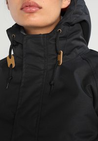 Czarna wodoodporna kurtka z wysokim kołnierzem, kapturem na sznurku i akcentami w kolorze złotym. Teksturowany materiał i regulowane sznurki.