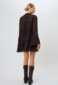 Vestido de leopardo en negro y marrón con mangas largas, diseño en capas, textura fluida y cierre de botones en la parte posterior, combinado con botas marrones hasta la rodilla.