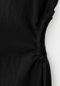 Tissu noir avec couture latérale froncée et cordon ajustable créant un détail froncé.