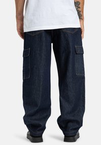 Tmavomodré cargo nohavice s širokými nohavicami, dvoma bočnými vreckami a kontrastným šitím. Tkanina má hladkú textúru s minimálnym leskom.