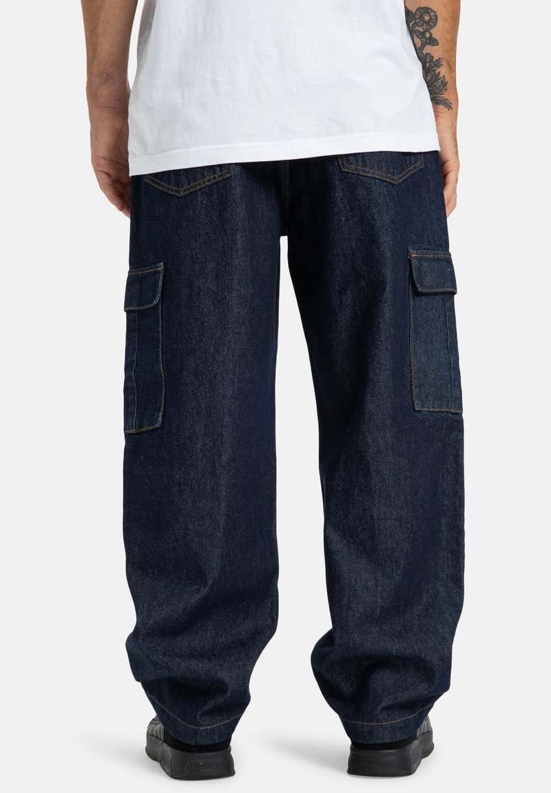 Tmavomodré cargo nohavice s širokými nohavicami, dvoma bočnými vreckami a kontrastným šitím. Tkanina má hladkú textúru s minimálnym leskom.