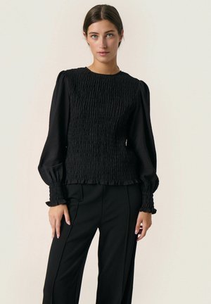 Black smocked top with long puff sleeves, textured fabric, and ruffled cuffs, paired with fitted black trousers. Simple design, no patterns.