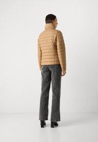 Beige pufferjakke med horisontale quiltede detaljer, høj krave, parret med grå brede jeans og sorte sko med blokhæle.
