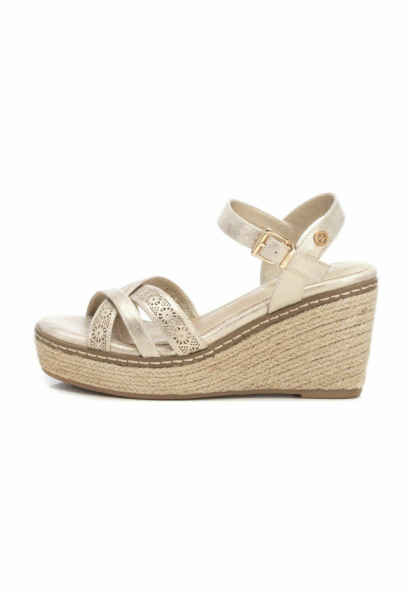 Sandalia de cuña beige con suela de esparto texturizada, correas entrelazadas y correa de tobillo ajustable. Presenta un patrón decorativo de recortes.