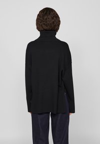 Μαύρο πουλόβερ τύπου ζιβάγκο με χαλαρή εφαρμογή, μαλακή υφή και πέφτοντους ώμους. Εχει πλαϊνές σχισμές και ραμμένο γιακά.