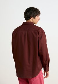 Μαρούλι μακρυμάνικο πουκάμισο με γιακά με κουμπιά, πίσω πτυχές και μανσέτες με δύο κουμπιά, σε συνδυασμό με ροζ παντελόνι. Λείο υφασμάτινο υλικό.