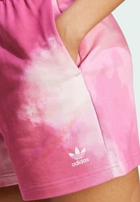 Shorts sportivi rosa realizzati in tessuto morbido con un motivo tie-dye. Comprendono tasche e un logo bianco adidas vicino all'orlo.