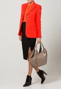 Blazer rojo, blusa naranja, falda lápiz negra con abertura lateral, botines negros y bolso beige con acentos dorados.