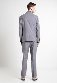Costum gri cu un model discret în carouri, sacou cu două butoane și pantaloni cu față dreaptă. Textură de țesătură netedă și rever cu zimți.