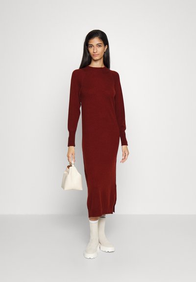 Vestido tricotado em bordô com mangas compridas, punhos canelados e fendas laterais. Combinado com botins brancos e uma pequena bolsa branca. Textura suave.