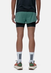 Grüne Shorts, die über schwarzen Kompressionsshorts getragen werden, weiße Socken mit schwarzen Streifen und mehrfarbige Schuhe mit strukturiertem Obermaterial und grünen Akzenten.