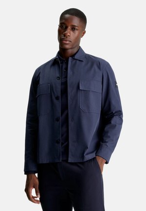 Giacca blu navy in misto cotone, caratterizzata da una chiusura con bottoni, due tasche sul petto e maniche lunghe. Tessuto morbido con una vestibilità moderna.