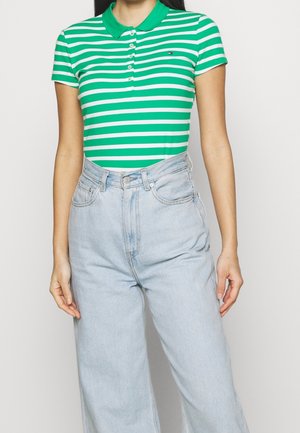 Mujer que lleva una camisa tipo polo de manga corta con rayas verdes y blancas, metida dentro de unos vaqueros de pierna ancha de talle alto de color azul claro.