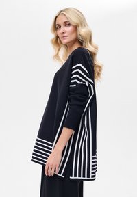 Granatowy sweter z białymi paskami. Luźny krój z okrągłym dekoltem, długimi rękawami i bocznymi rozcięciami dla większego komfortu.