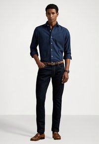 Granatowa koszula na guziki z wzorzystym kołnierzykiem, ciemne dżinsy, czarny skórzany pasek i brązowe skórzane buty. Szykowny, casualowy krój, gładka faktura.