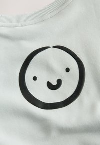 Tissu gris clair avec une texture lisse présentant un motif circulaire noir. Le motif représente un visage souriant minimaliste avec des yeux et une bouche.