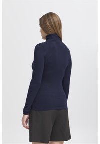 Mornarica turtleneck džemper s dugim rukavima, prilagođenog kroja, rebrastog ovratnika i šava, u kombinaciji s tamnom suknjom, ravne teksture, s minimalnim detaljima.