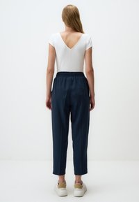 Witte geribde top met korte mouwen en een V-hals, gecombineerd met donkerblauwe taps toelopende broek met een elastische tailleband en zijzakken.