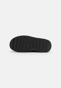 Semelle de chaussure en caoutchouc noir avec texture striée et bout arrondi. La section du talon est légèrement surélevée avec des détails de marque. Taille 37 indiquée.