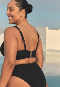 Schwarzes Bikini-Set mit verstellbaren Trägern, goldenen Hardware-Details und hoch sitzendem Höschen. Glattes, strukturiertes Material mit minimalen Verzierungen.