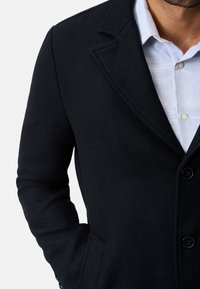 Black wool coat with a notched collar, single-breasted design, and two-button closure. Textured fabric and side pockets are visible.
