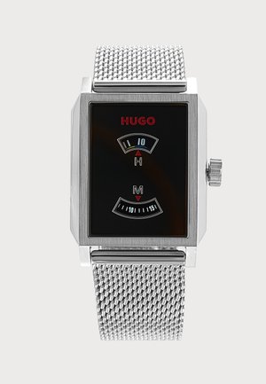 Montre-bracelet à bracelet en maille argentée avec cadran rectangulaire noir, logo rouge "HUGO" et double affichage numérique pour les heures et les minutes.