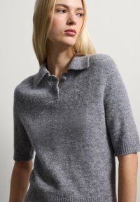 Grau gehäkeltes Poloshirt mit kurzen Ärmeln, aus weichem, strukturiertem Stoff. Verfügt über einen klassischen Kragen und einen gerippten Saum, designed für eine entspannte Passform.
