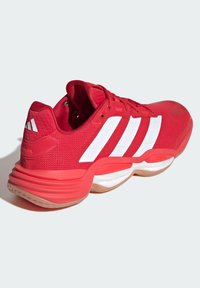 Red athletic shoe with a mesh upper, white three-stripes design, rounded heel, and textured rubber sole for enhanced grip and support.