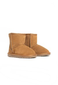 Botas de tobillo de ante color beige con un suave forro de piel, punta redondeada y suela de goma plana. Presenta detalles de costura y un diseño sencillo.
