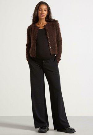 Cardigan marrone delicato sopra una maglietta nera, abbinato a pantaloni neri a gamba larga e scarpe nere; presenta bottoni sulla parte anteriore e una finitura testurizzata.