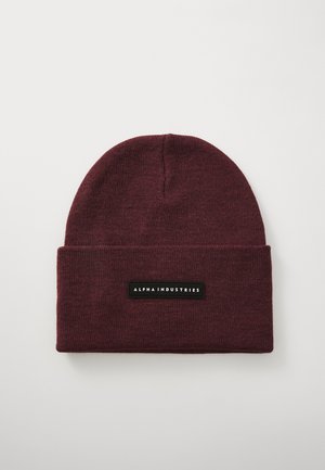 Burgundy knit beanie with folded cuff featuring a rectangular black patch labeled "Alpha Industries" on a white background.