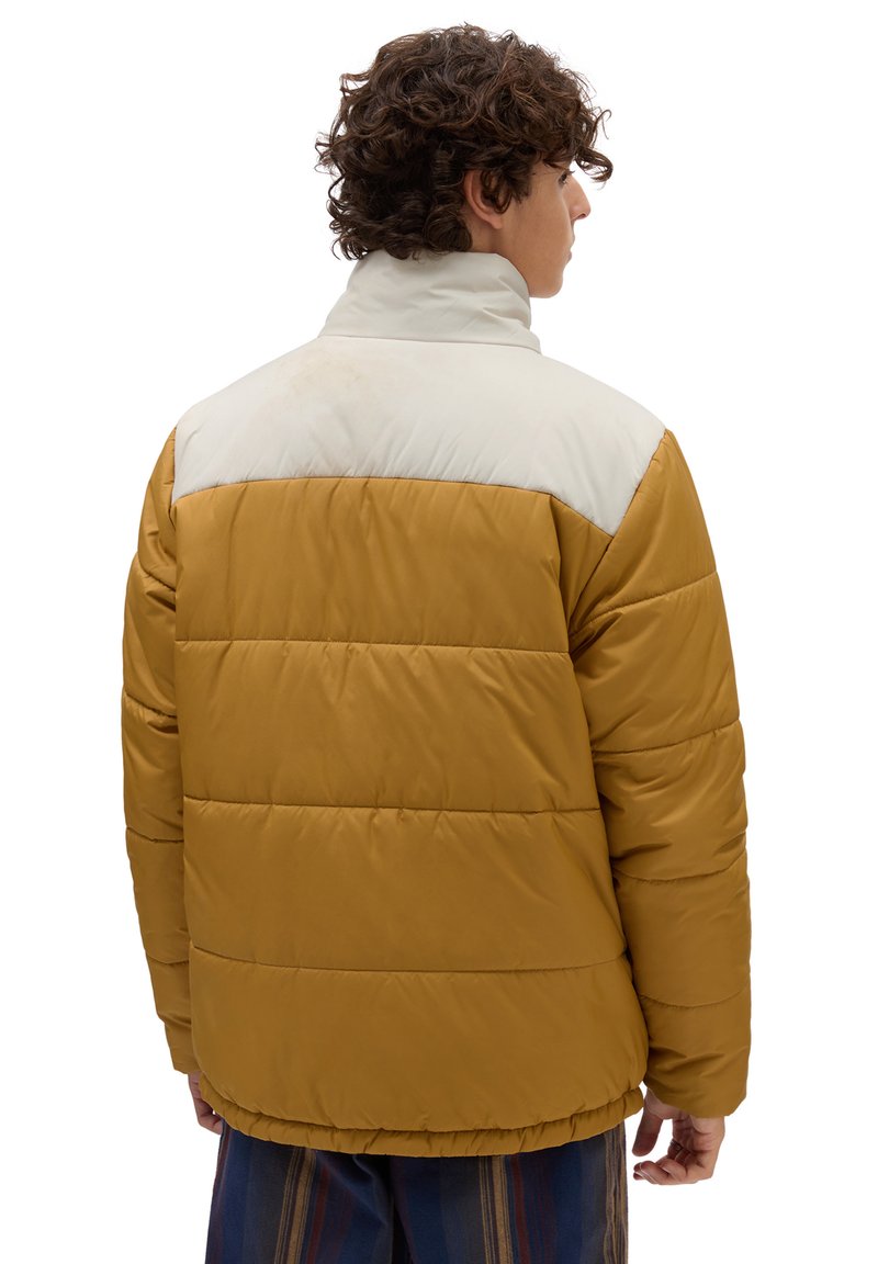 Veste matelassée avec un design bicolore, la partie inférieure étant jaune moutarde et la partie supérieure blanche. Col avec une texture lisse.