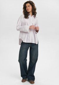 Striped button-up shirt in light pink and white, paired with dark blue wide-leg jeans. Features long sleeves and relaxed fit. Brown shoes.