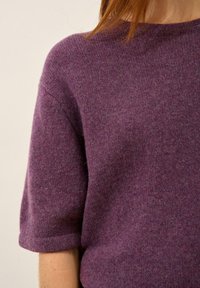 Fioletowy sweter dzianinowy z krótkimi rękawami, o miękkiej fakturze i okrągłym dekolcie. Materiał wydaje się delikatny i lekko melanżowy.