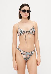 Blommig bikiniuppsättning med ett mönstrat överdel och justerbar knytning samt matchande underdel, tillverkad av mjukt tyg i en blandning av pastellfärger.