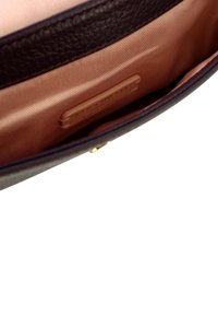 Pochette en cuir marron à la texture lisse, doublure intérieure crème et accent en métal doré. Étiquette de marque notable visible à l'intérieur.