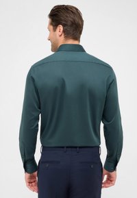 Camicia a maniche lunghe di un verde scuro, con una texture liscia e polsini abbottonati. La parte posteriore presenta un colletto classico e una vestibilità sartoriale.