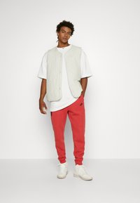 Gaisā, quiltēta veste, balta oversize T-kreklu, sarkani sporta bikses, baltas sporta kurpes, ar Nike logo uz vestes un biksēm. Neitrālas krāsas un brīva piegriezuma.
