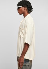 Chemise crème à manches courtes en tissu léger, dotée d'une poche sur la poitrine et d'une coupe décontractée, associée à un pantalon cargo en denim clair.